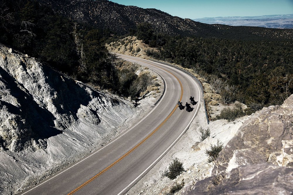 A distant shot of 3 cruiser motorcycles taking a long sweeping corner on the road with pine trees along each side