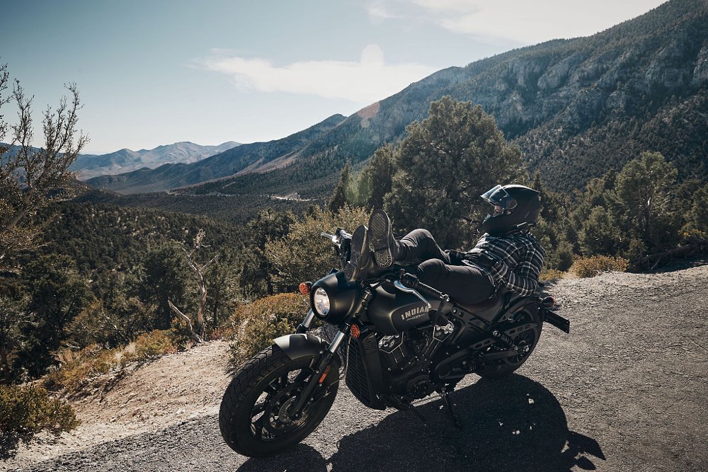 A female rider is reclined on the Indian Scout Bobber enjoying a scenic mountain vista.