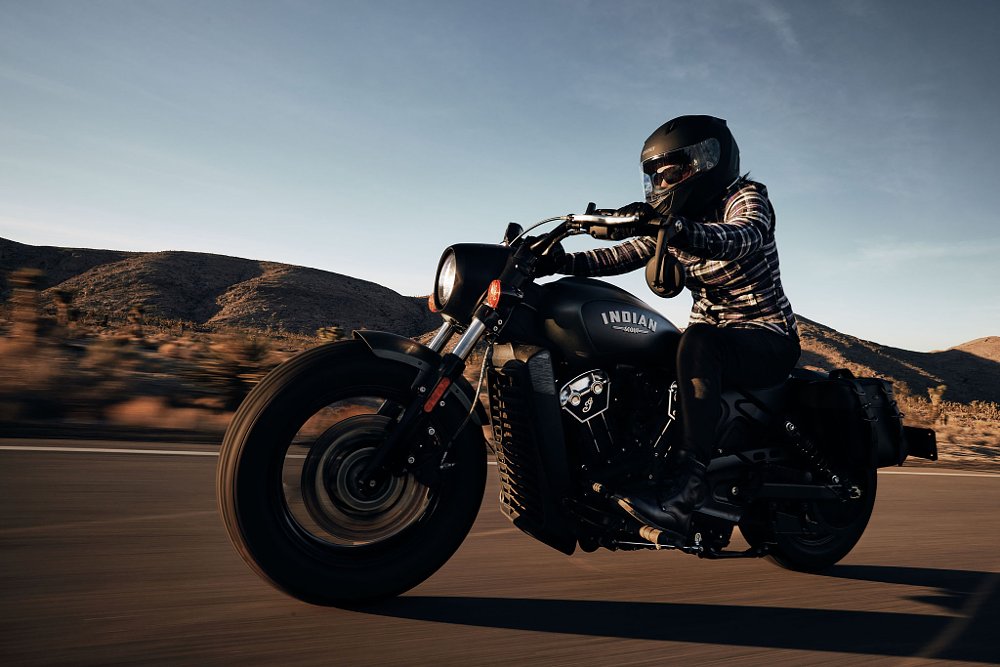 A side profile panning shot of the Indian scout Bobber in motion on open desert road with blue skies
