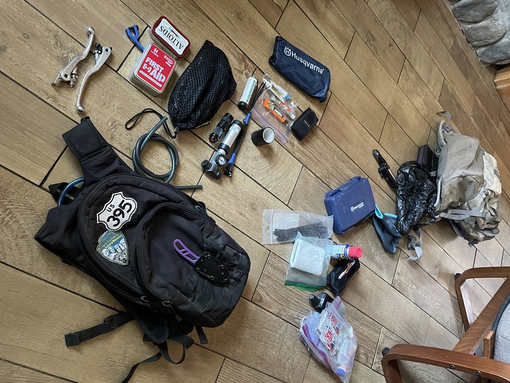 Two packs full of spare parts and repair kits are strewn on the hard wood floor of a cabin.