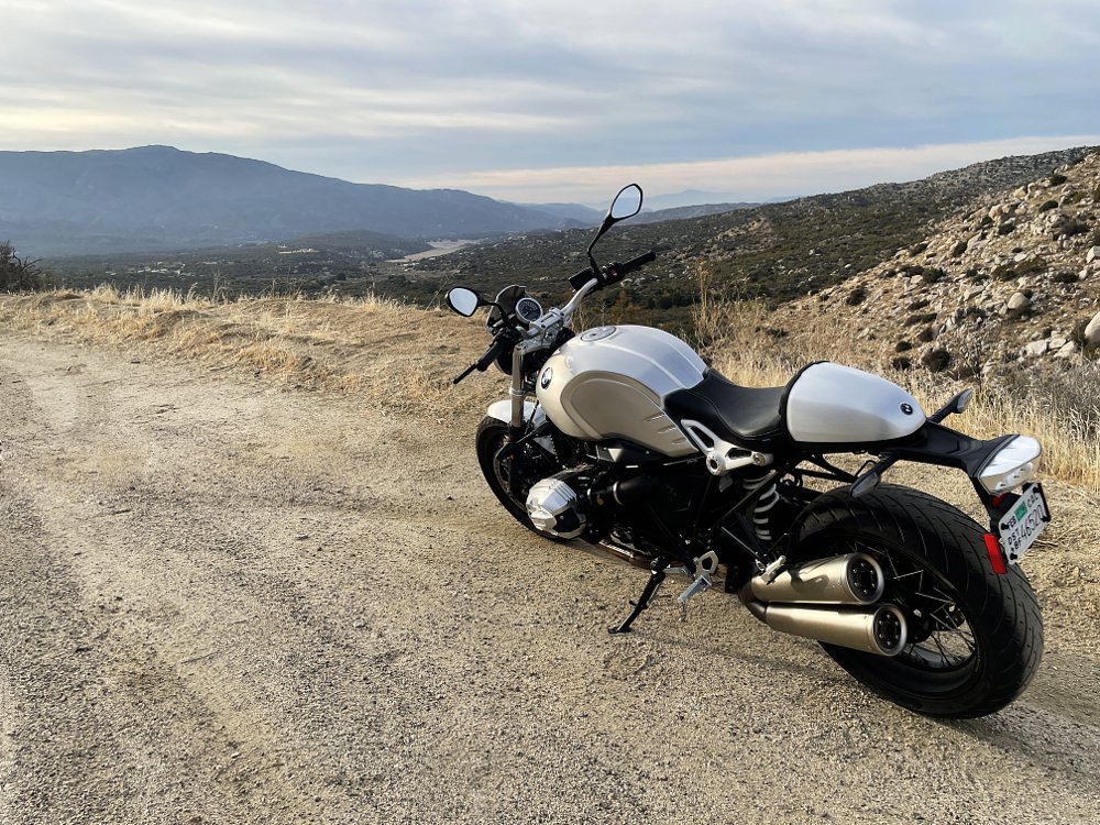 A rear 3/4 view of the BMW R nineT Pure motorcycle perched on a cliffside vista