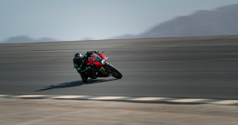A female rider is dragging knee in a fast corner on board the Speed Triple 1200 RR on a race track
