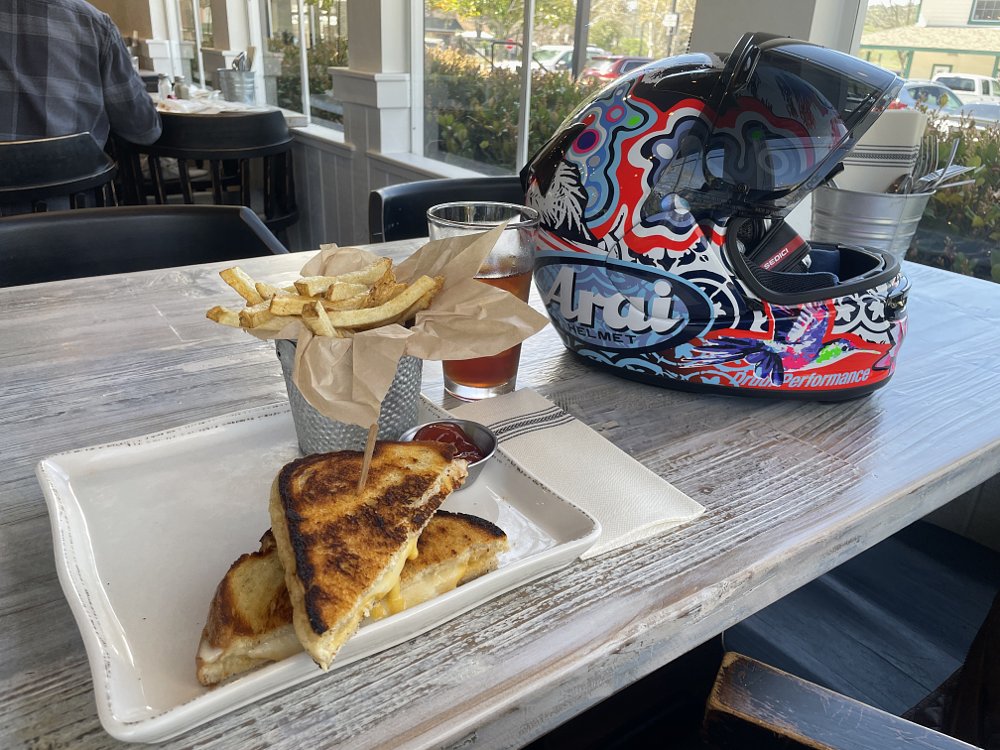 A photo of a grilled cheese sandwhich, fries, and Arai helmet in a nice farmhouse style restaurant