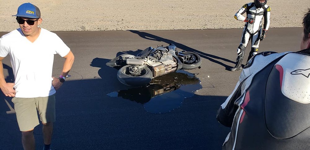 A group of flag marshals gather around a fallen motorcycle on track that is leaking oil