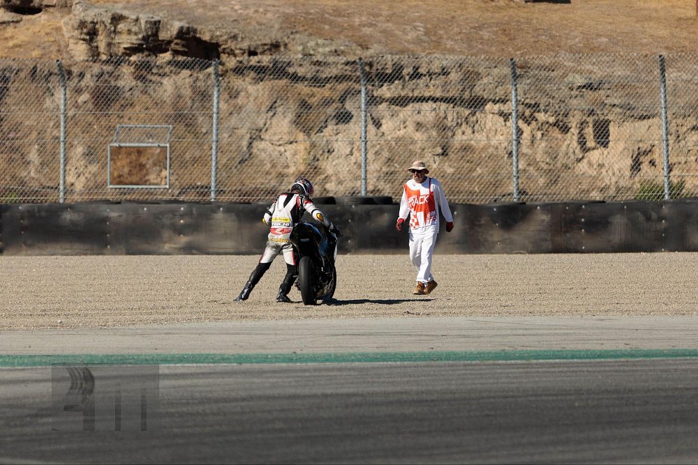 A flag marshal comes running out to help a motorcycle racer with his crashed bike