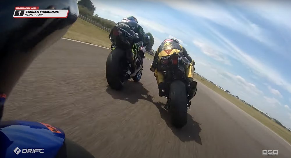 Onboard view of a British Superbike race, with two motorcycles just ahead at speed.