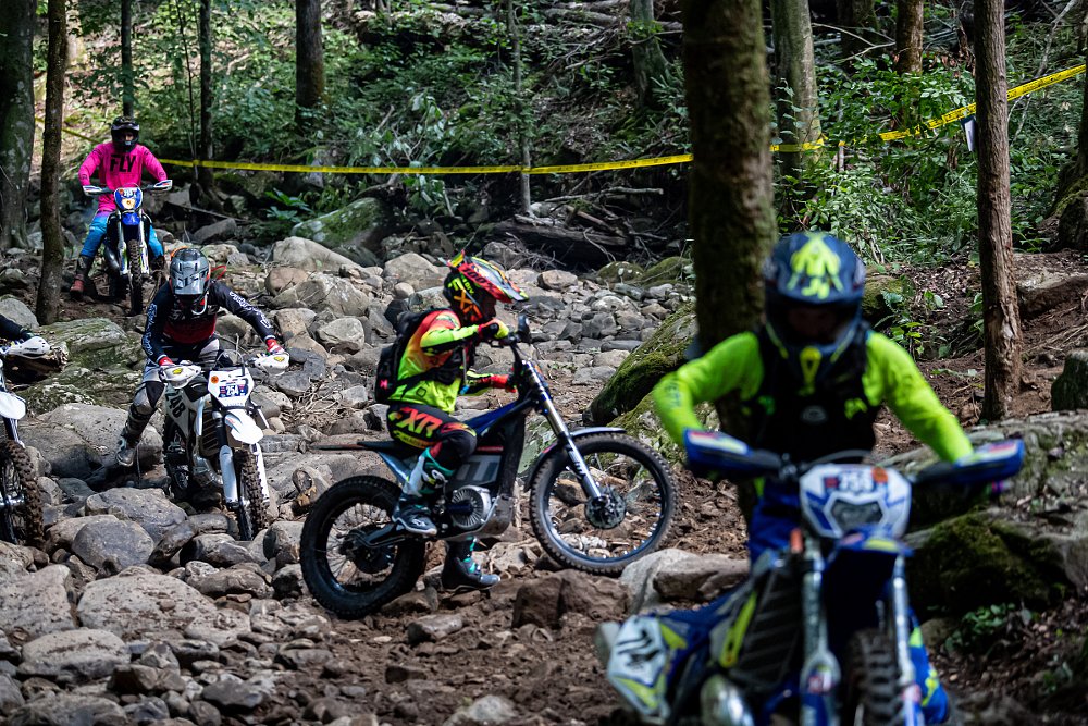 motorcycles riding through a rocky section in the woods