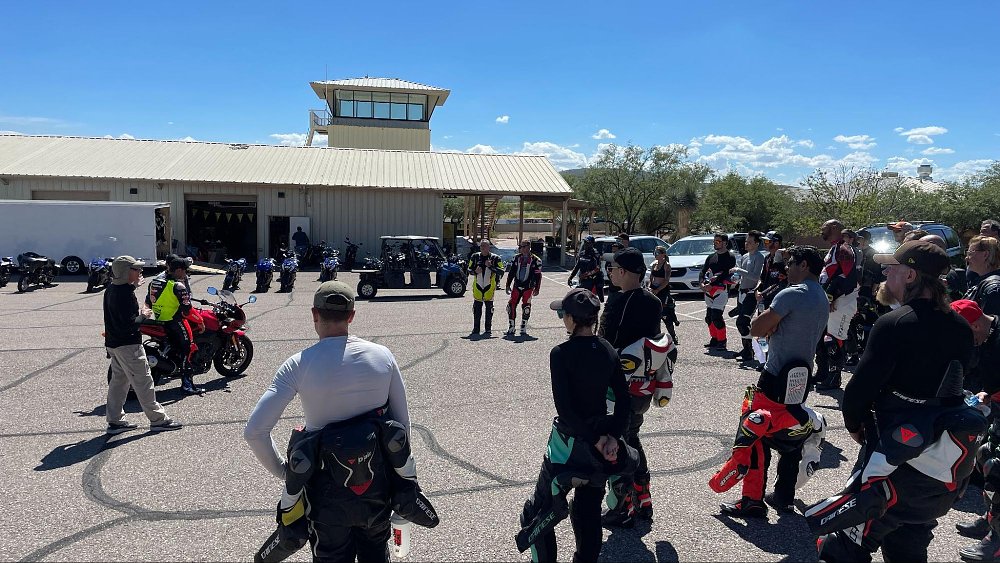 A group of students gather around a motorcycle and a coach for a lesson