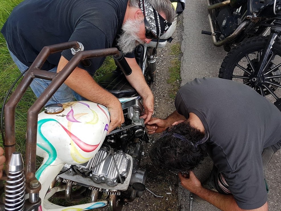 two men working on an old chopper at roadside