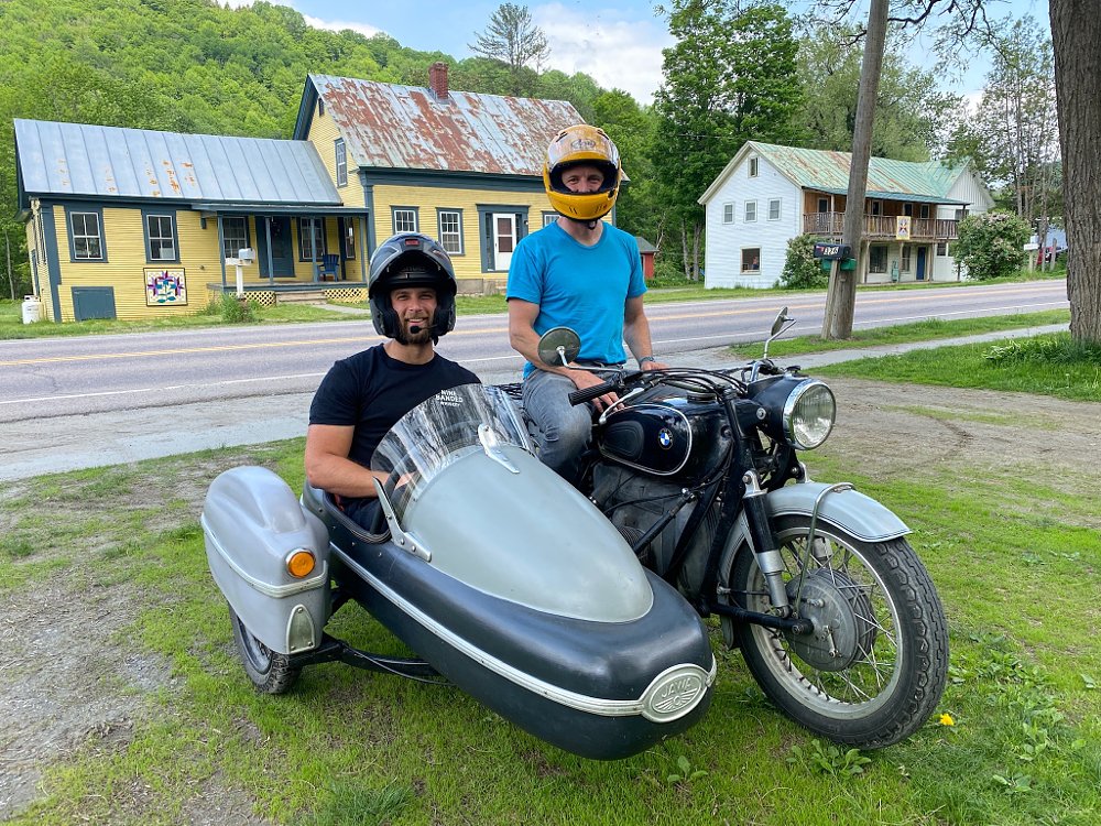 A vintage BMW sidecar with a rider and passenger on board, posing in a small town.