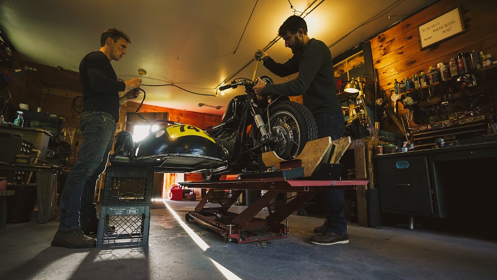 Ari and Zack working on a vintage racing sidecar in a dark garage.