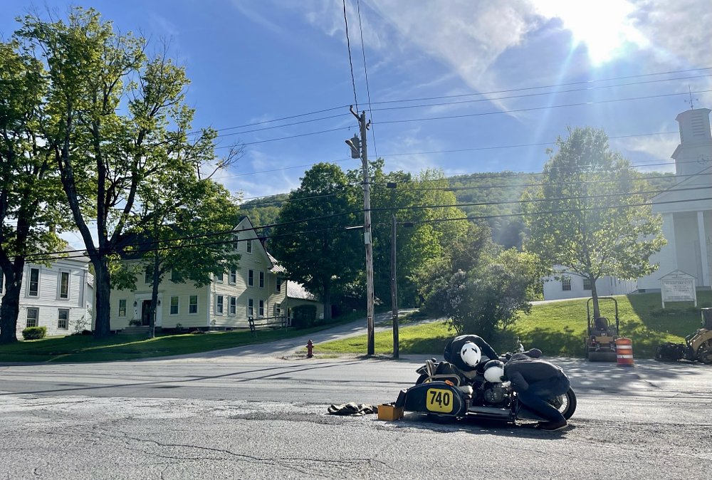 Two men working on a sidecar in a small town.