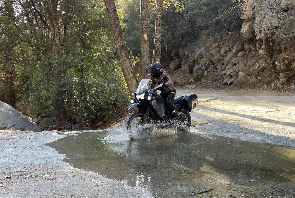 A female rider pilots the full size KLR650 Adventure bike through a river water crossing