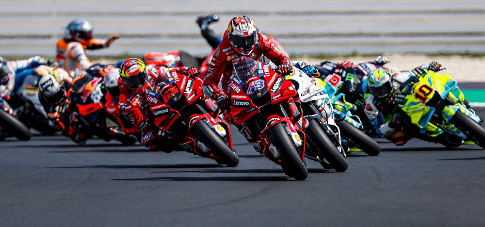 MotoGP field racing with riders crashing in the background
