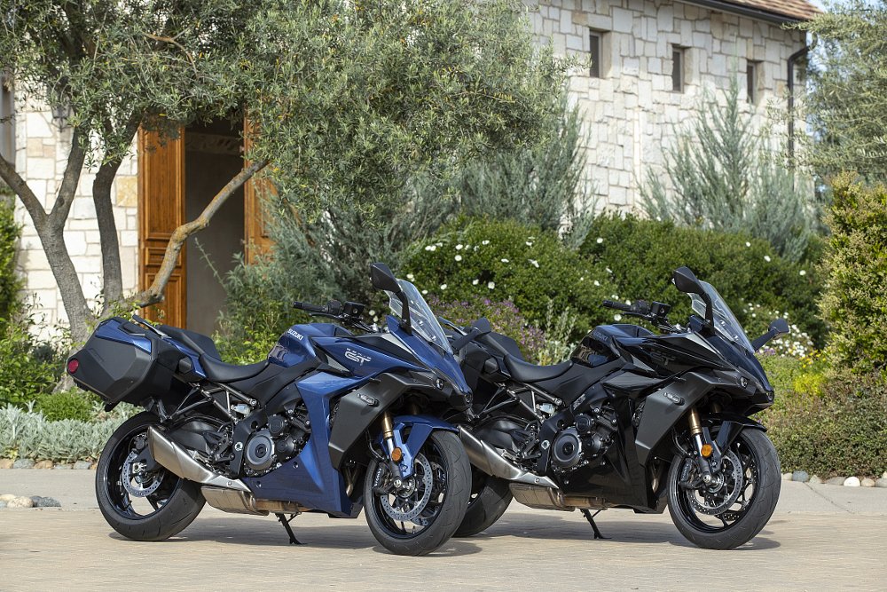 Two Suzuki GSX-S1000GT+ motorcycles parked in front of a stone building