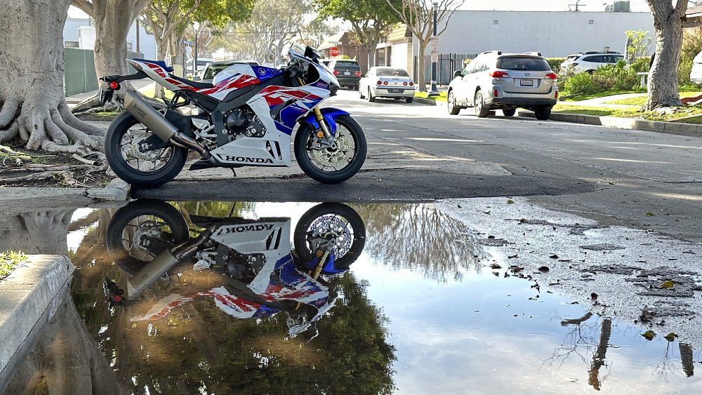 2022 Honda CBR1000RR-R SP reflecting in a puddle on a suburban street.