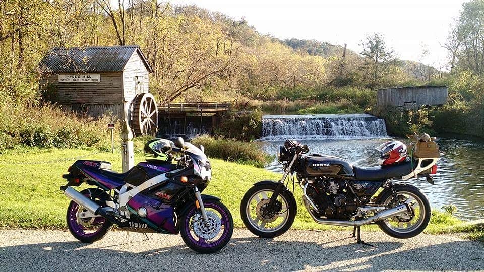 vintage motorcycles parked in front of a scenic old mill