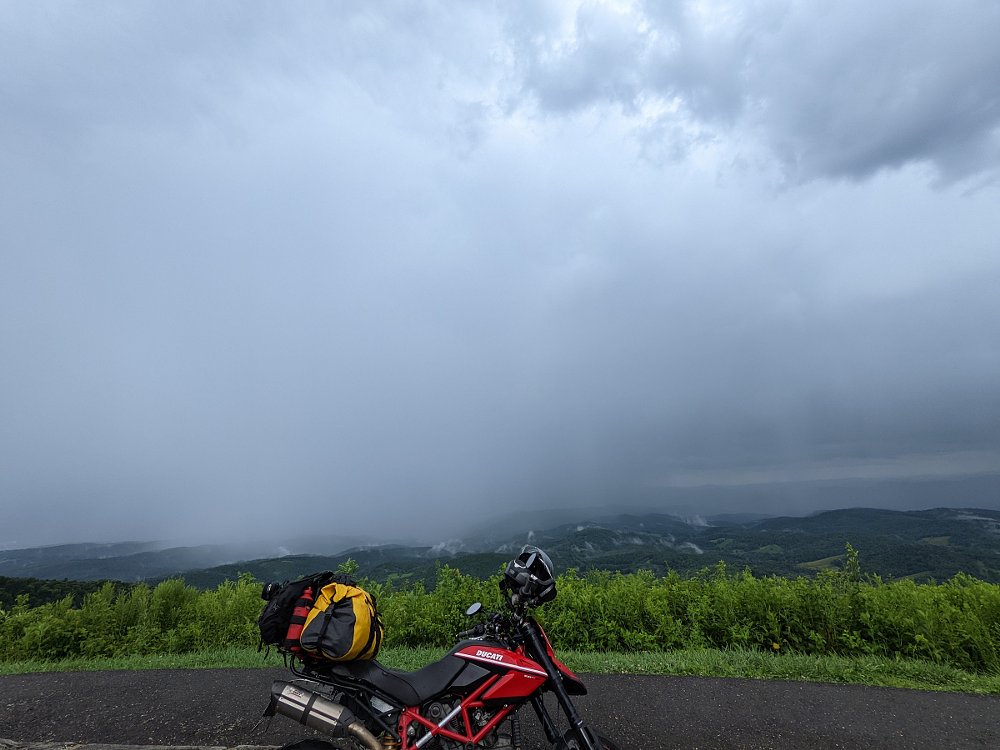 Ducati parked at a mountain overlook with heavy rain in the distance