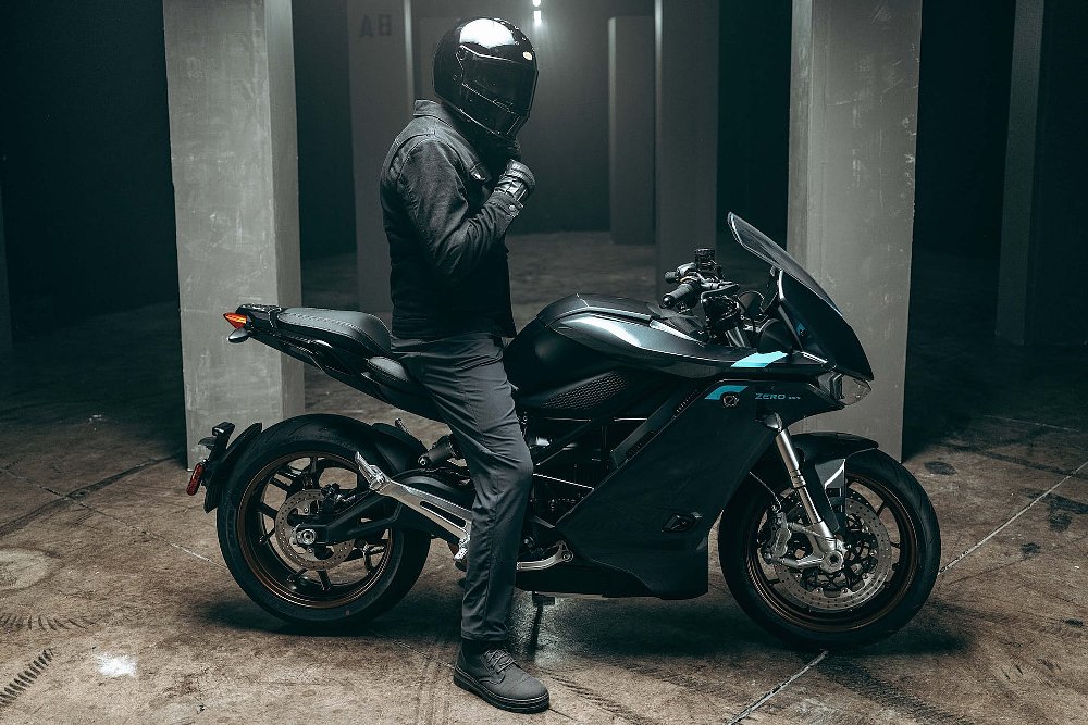 Side view of the Zero sr/s electric sportbike with a male street rider sitting on it in a garage