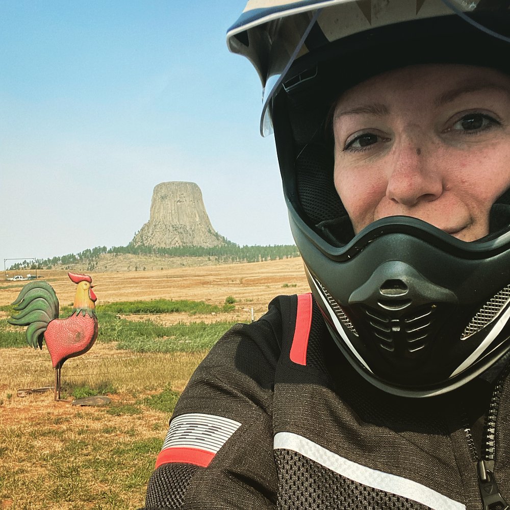 A photo of female rider Amanda taking a selfie in front of Devils Tower with helmet and riding gear on