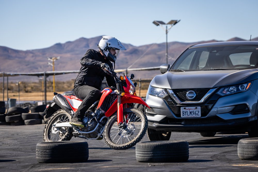 A Honda CRF300L navigates through a staged urban obstacle course in a parking lot.