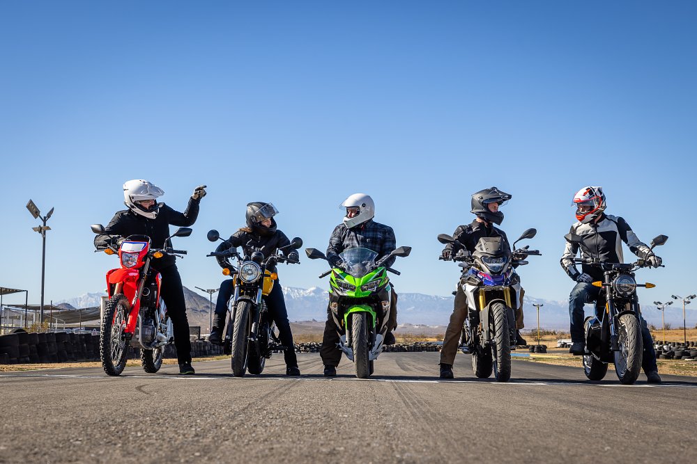 Five small motorcycles lined up at a starting line with riders aboard.