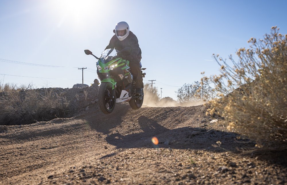 A Kawasaki Ninja 400 jumping over a dirt mount on a desert trail.