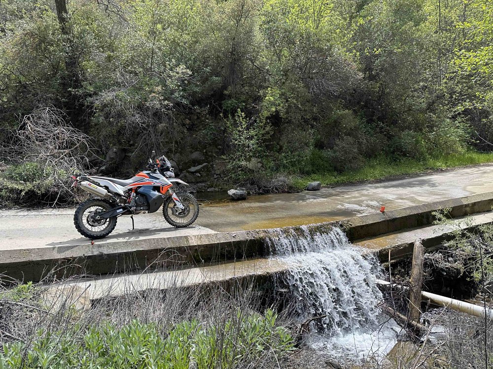 2021 KTM 890 Adventure R Rally parked just before a shallow stream running across a concrete wash in a mountain road.