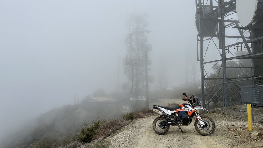 2021 KTM 890 Adventure R Rally parked on a gravel road, surrounded by fog and radio towers.
