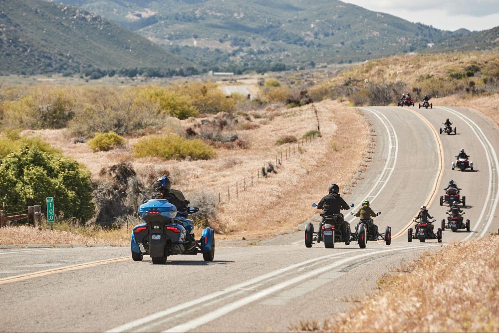 a rear view shot of the group of riders going down a country road on 3 wheel machines
