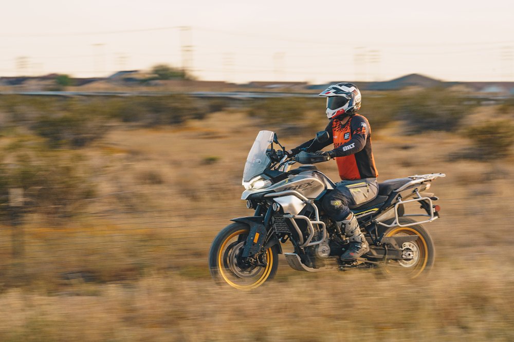 A CFMOTO Ibex 800 T from the left side, riding down a dirt road with the rider sitting.
