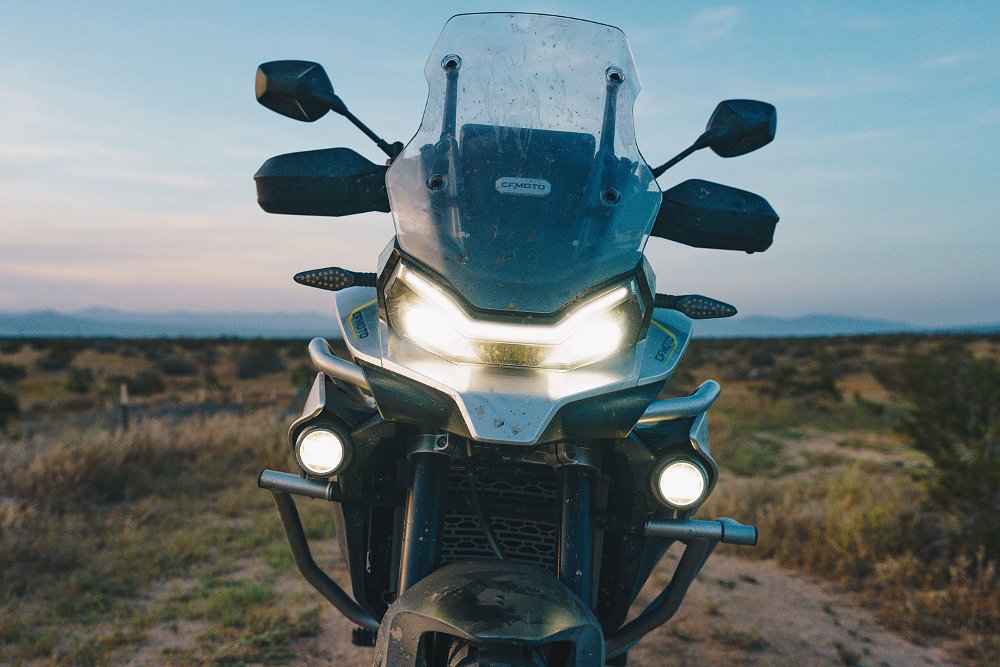 CFMOTO Ibex 800 T from the front, at dusk in the desert, with the headlights on.