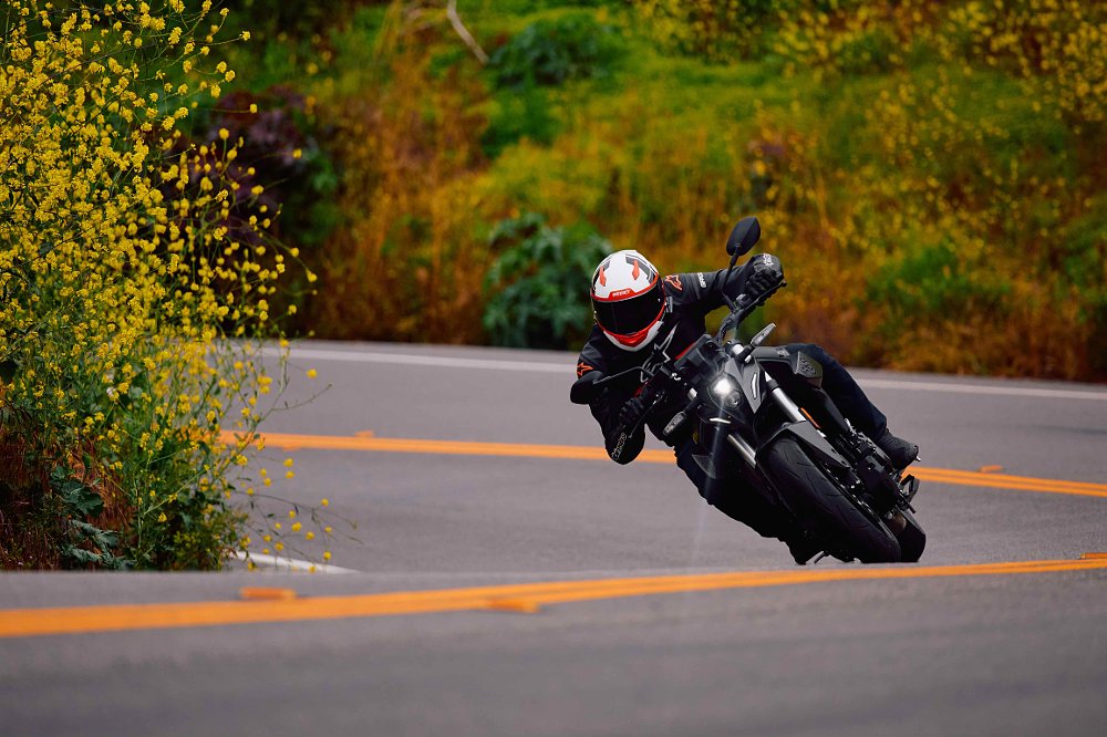2023 Suzuki GSX-8S riding through a right-hand turn, toward camera, with bright yellow wildflowers lining the inside of the turn.