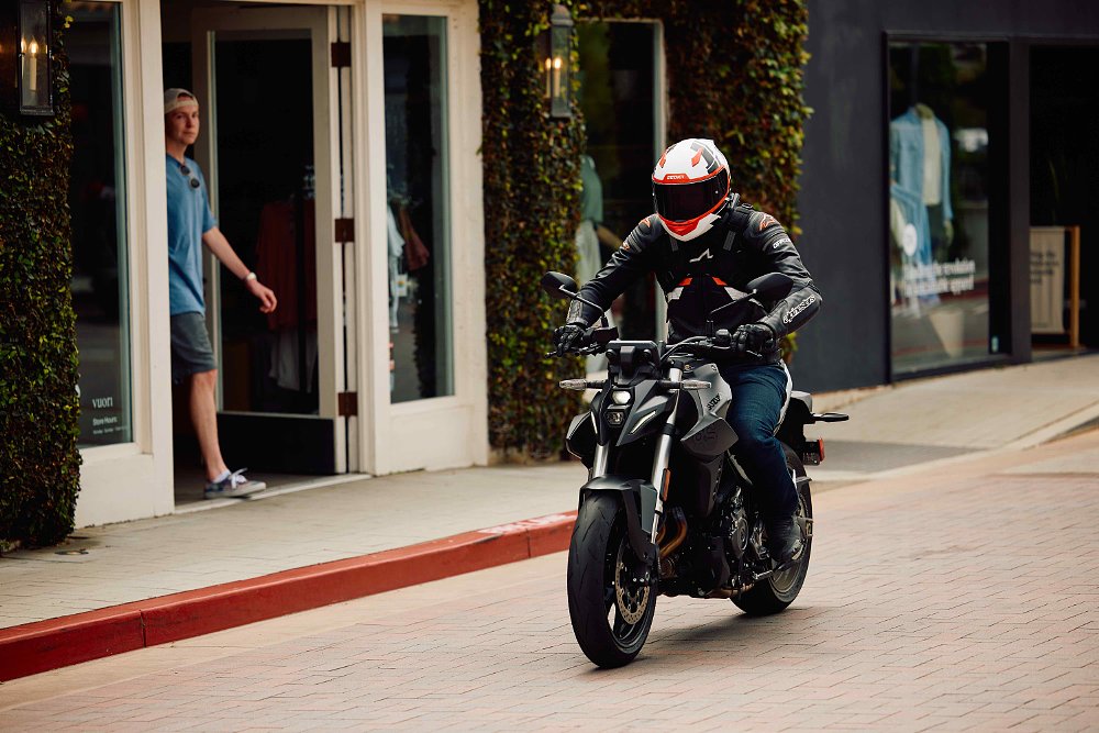 2023 Suzuki GSX-8S riding through an urban shopping area, with stores in the background.