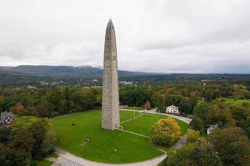A photo of Benington Battle Monument, it is a white stone obelisk jutting into a dark and stormy sky