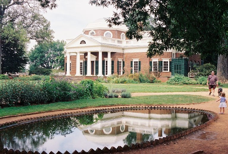 a photo of Monticello, that has brick facades and roman style columns in white, with a reflecting pond in front