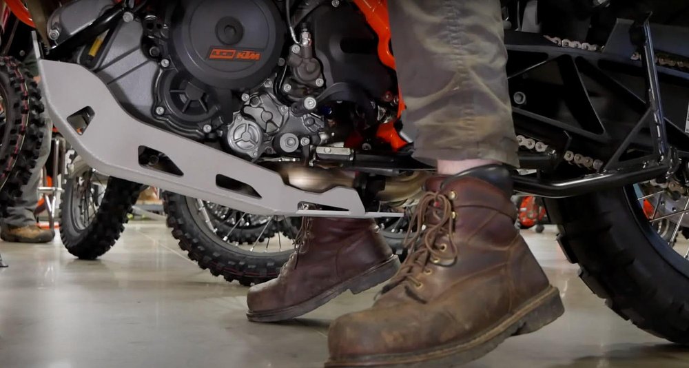a close up of brown work boots barely touching the ground on a KTM motorcycle