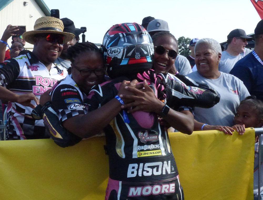 Mikayla Moore, still in leathers and helmet just off the track, is embraced by her family