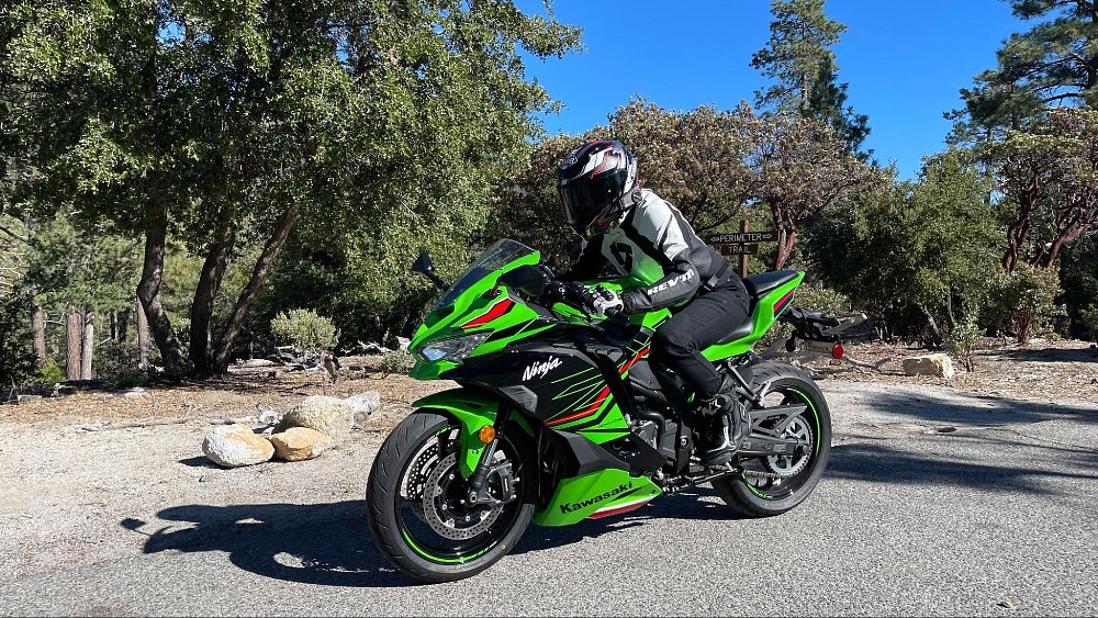 A female rider rides by the camera at slow speed on the zx-4rr in a pine forest