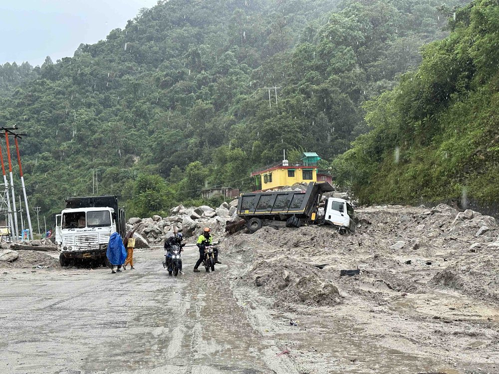 Two motorcyclists stop and look at a dump truck that has been turned on its side by a landslide near Pandoh, India.
