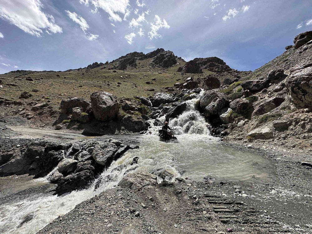A Triumph Speed 400 crosses a stream running across a road in the Ladakh region of India.