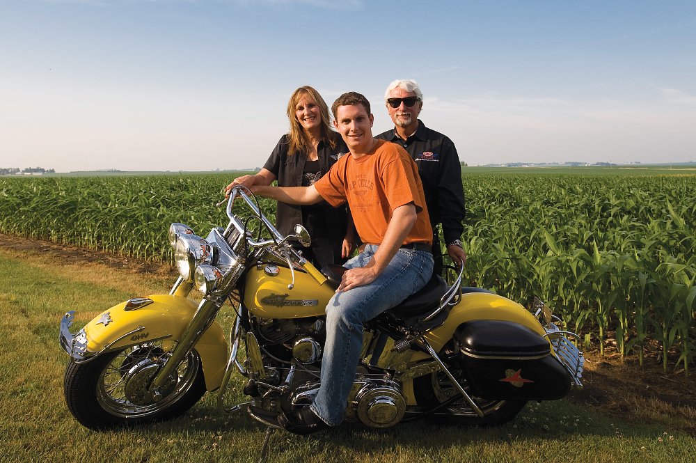 Zach Parham sitting on an old yellow Harley with his parents standing behind him