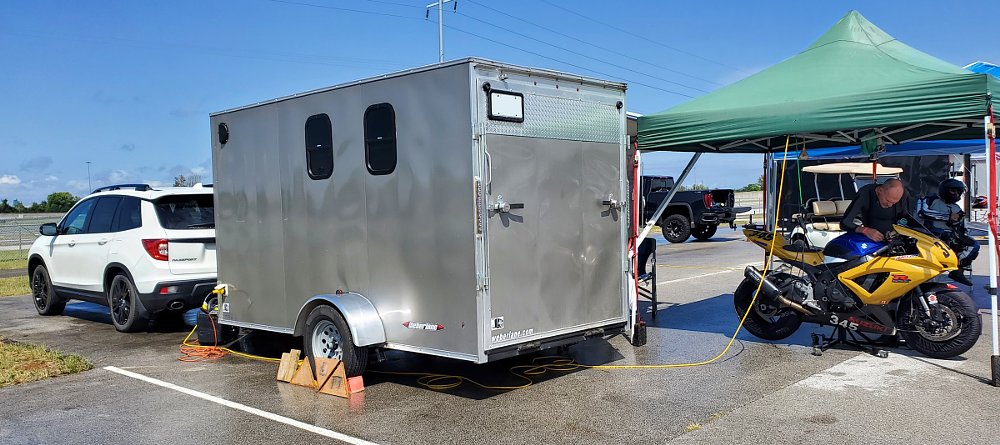 trailer set up in the race track paddock with the motorcycle under a pop-up canopy