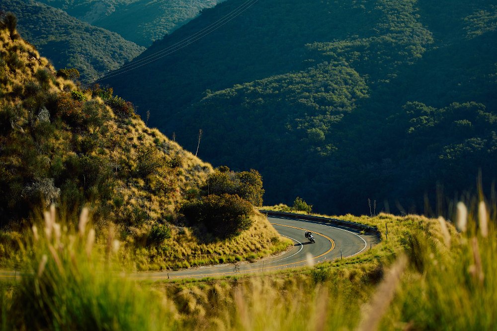 2023 Moto Guzzi V100 Mandello in the distance riding toward camera through a right hand turn on a mountain road