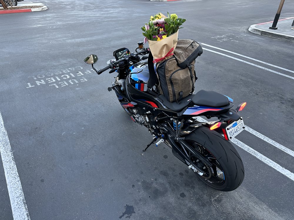 2023 BMW M 1000 R parked in a parking lot with a backpack resting on the seat.