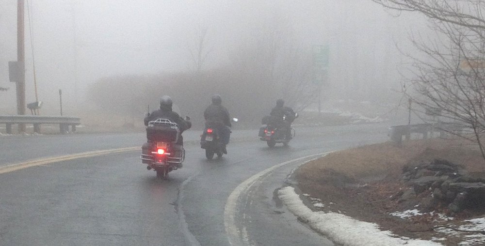 three riders on a wet road in the rain and fog