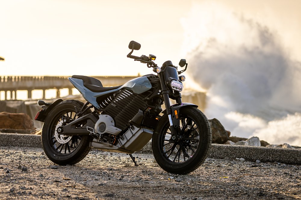 2024 LiveWire Del Mar parked near a jetty with a wave crashing in the background.
