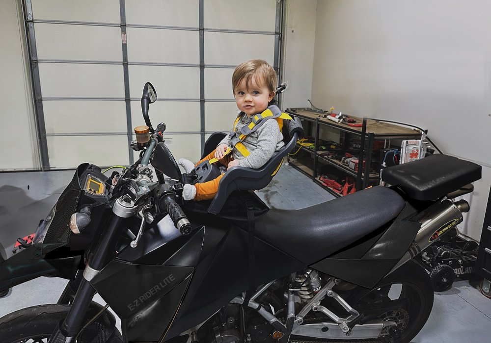 child on a car seat mounted on a motorcycle gas tank