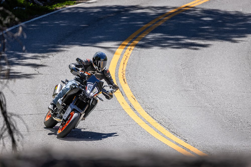 2024 KTM 890 SMT riding toward camera through a gentle turn on a mountain road.