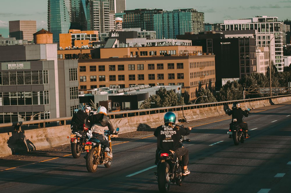 four riders on a city highway with buildings in the background